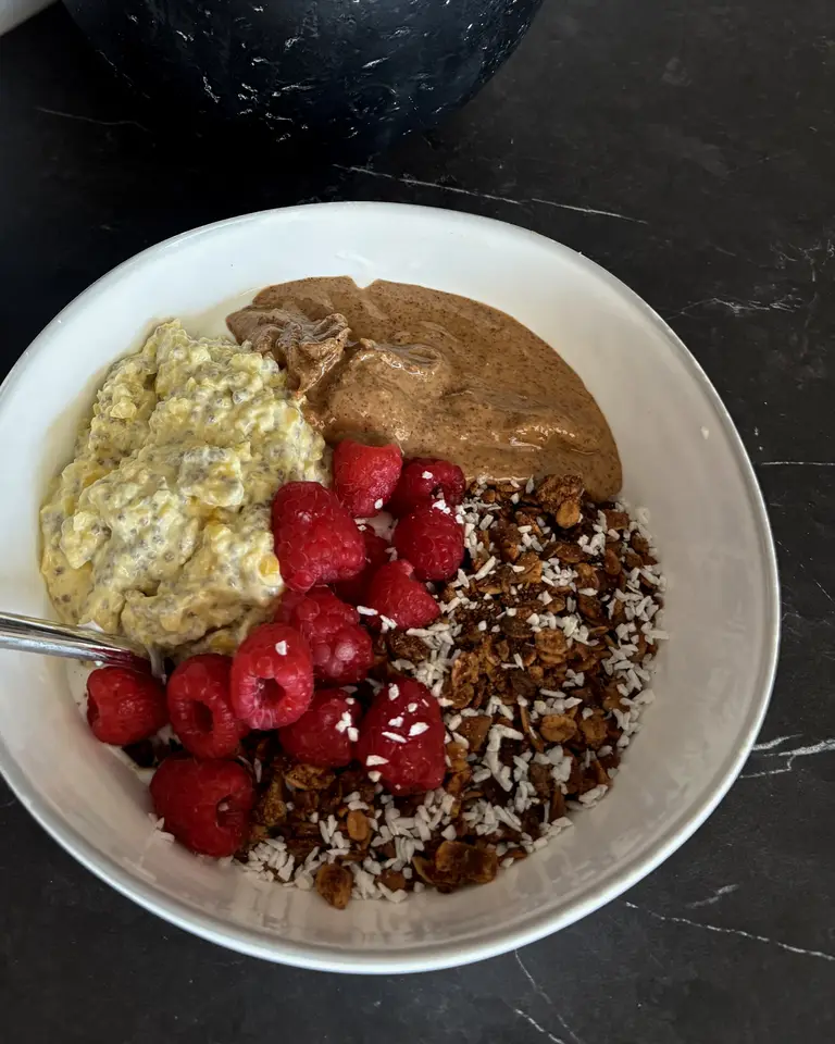 A Sante Organics bowl with chia pudding, raspberries, granola, coconut flakes and nut butter on a black marble counter